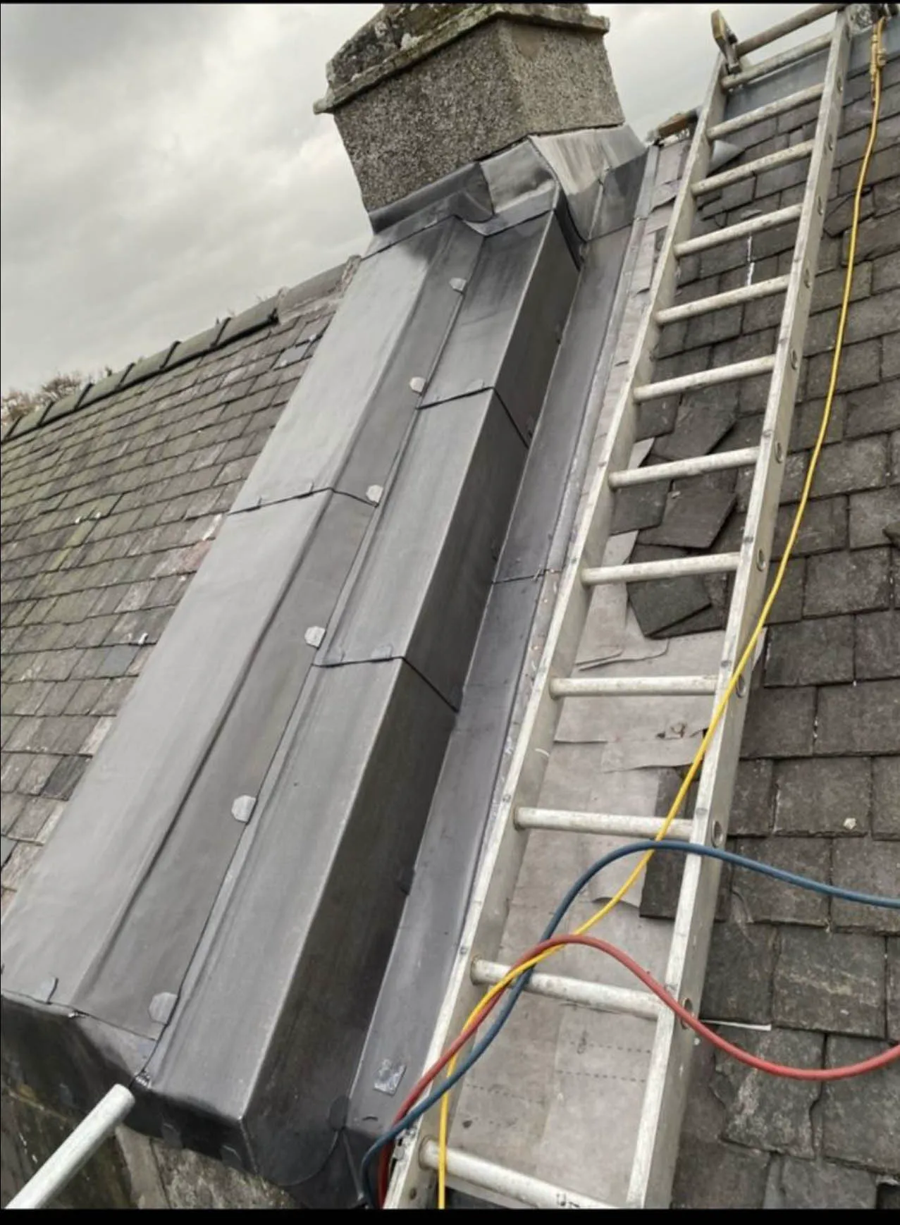 New lead valley running down a slate roof, with a ladder in place