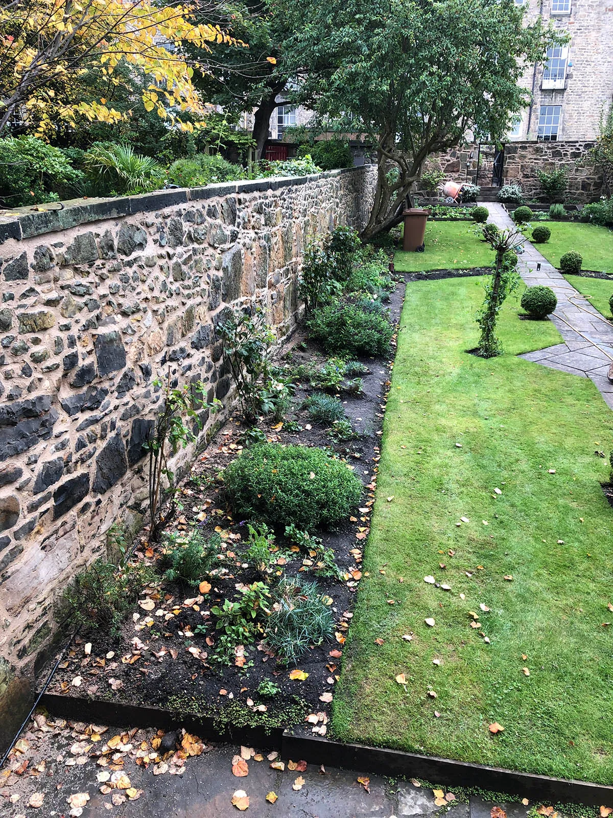 Long rubble stone garden wall beside a lawn after lime repointing