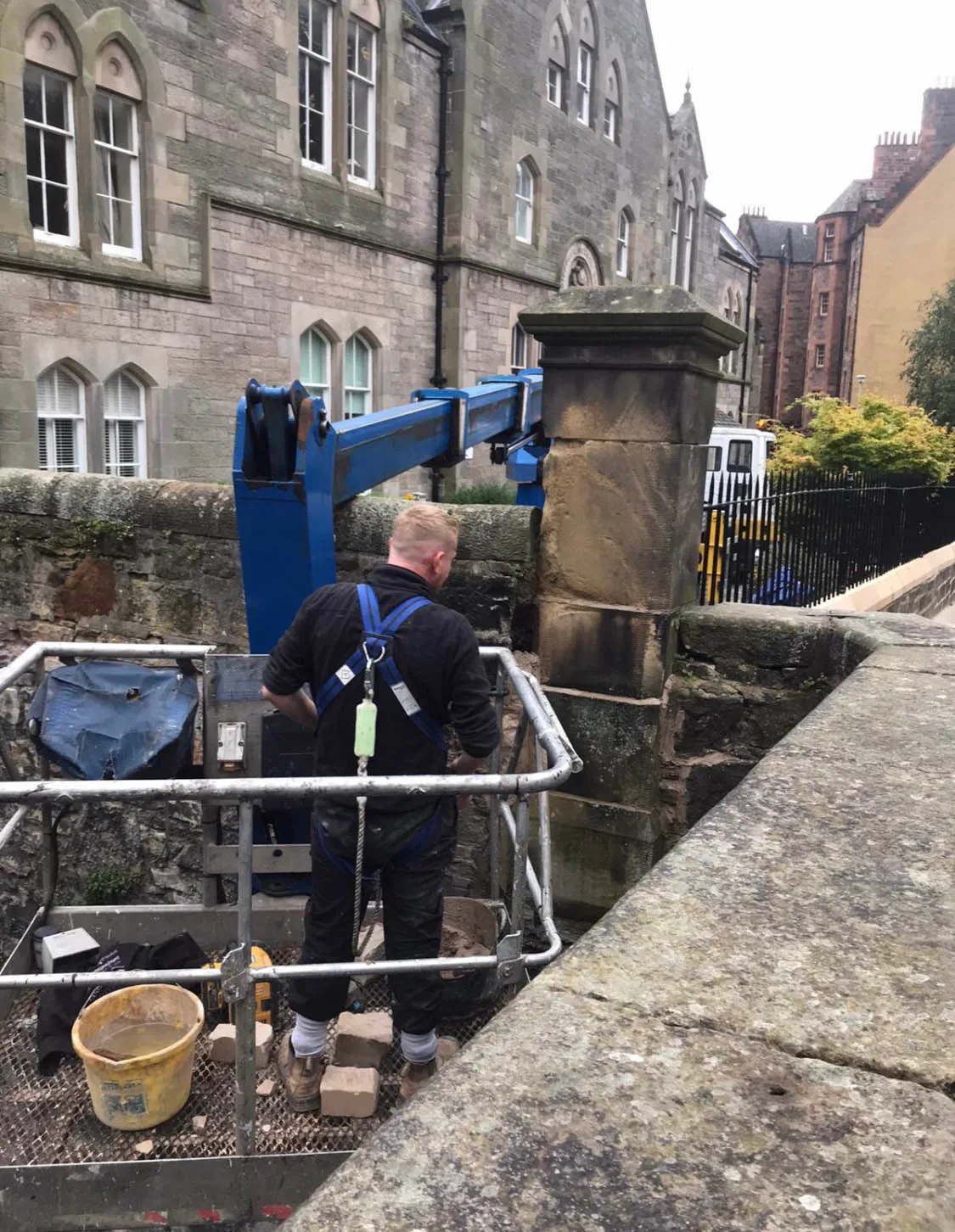 Stonemason working from a cherry picker platform on a stone gate pier