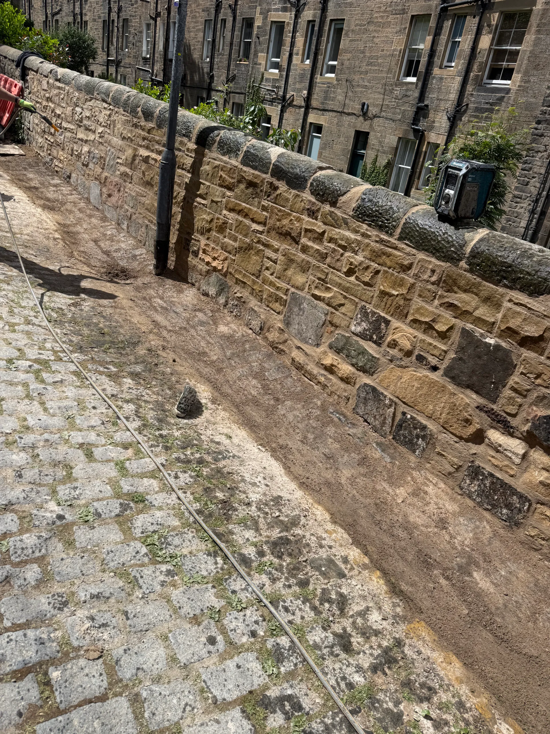 Repointed rubble stone boundary wall along a cobbled lane