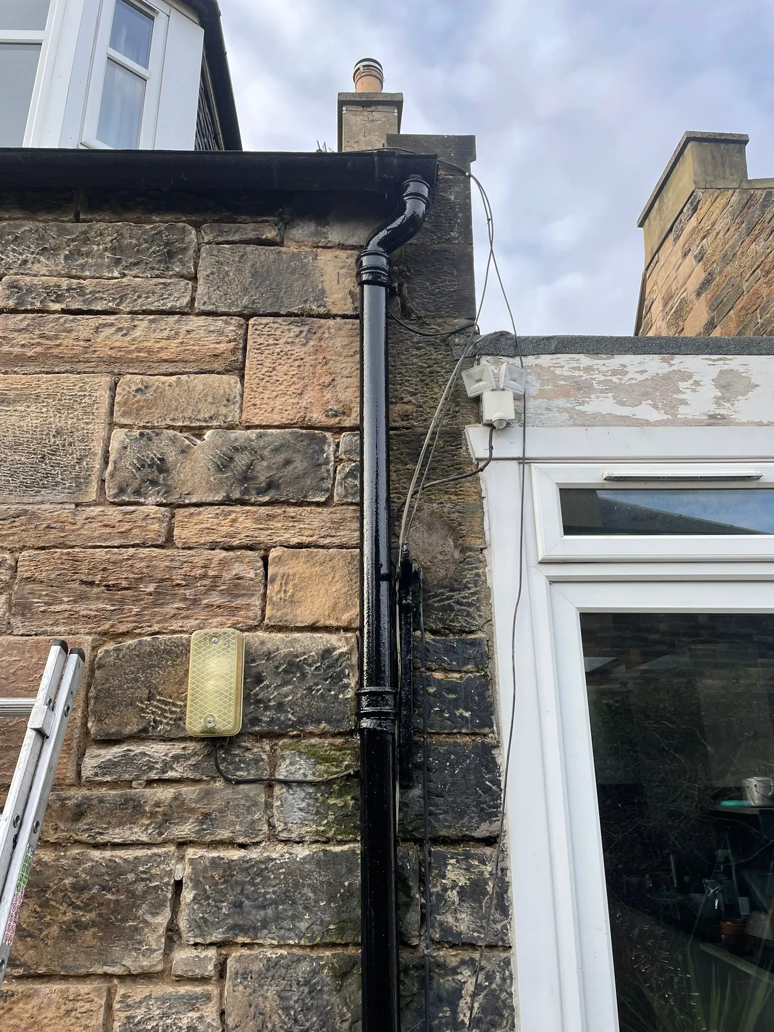 Cast iron downpipe on a sandstone wall beside a window