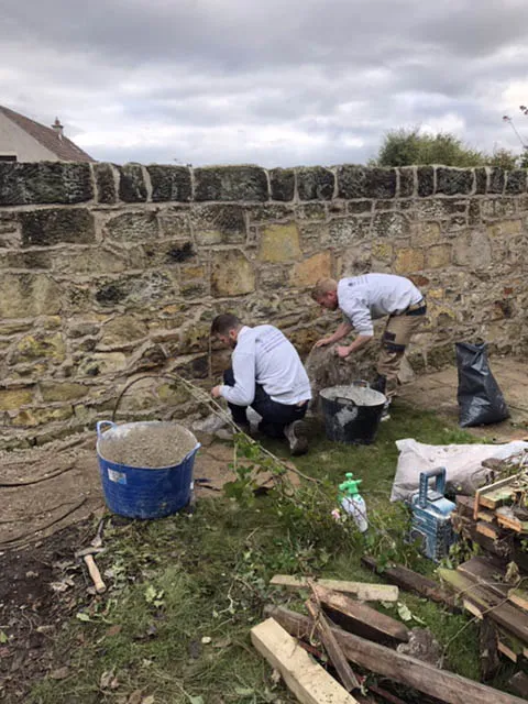 Stonemasons repointing a garden wall, mixing lime mortar on site