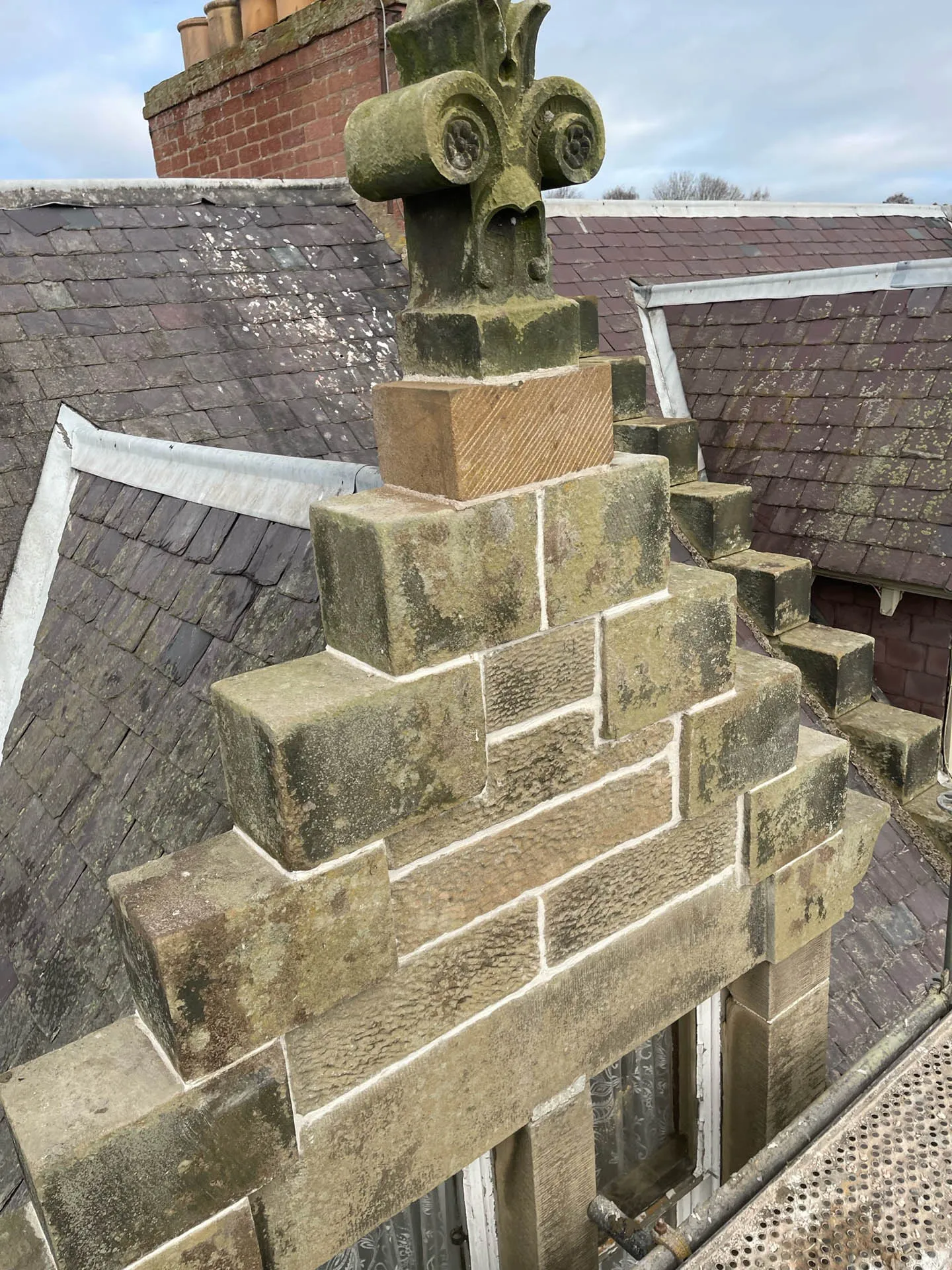Carved stone cross finial on a gable above a slate roof
