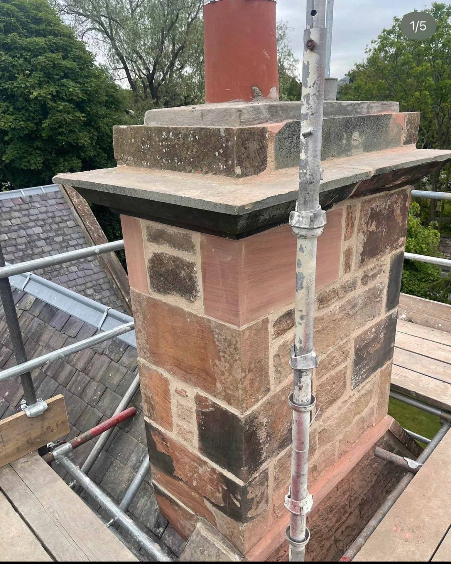 Red sandstone chimney stack under repair, with a scaffold pole alongside