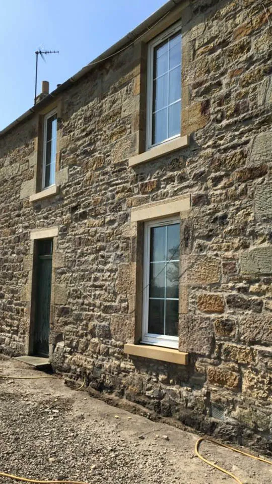 Repointed rubble stone gable wall of an Edinburgh house with white sash windows