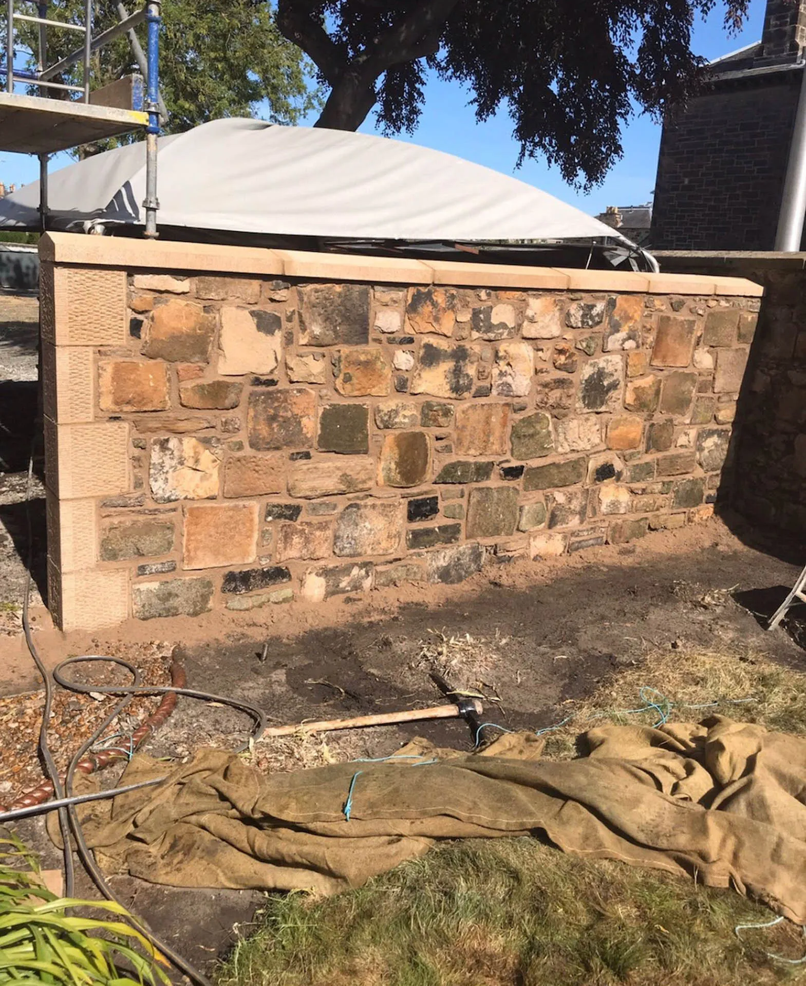Newly rebuilt stone wall with coping stones, under a tree