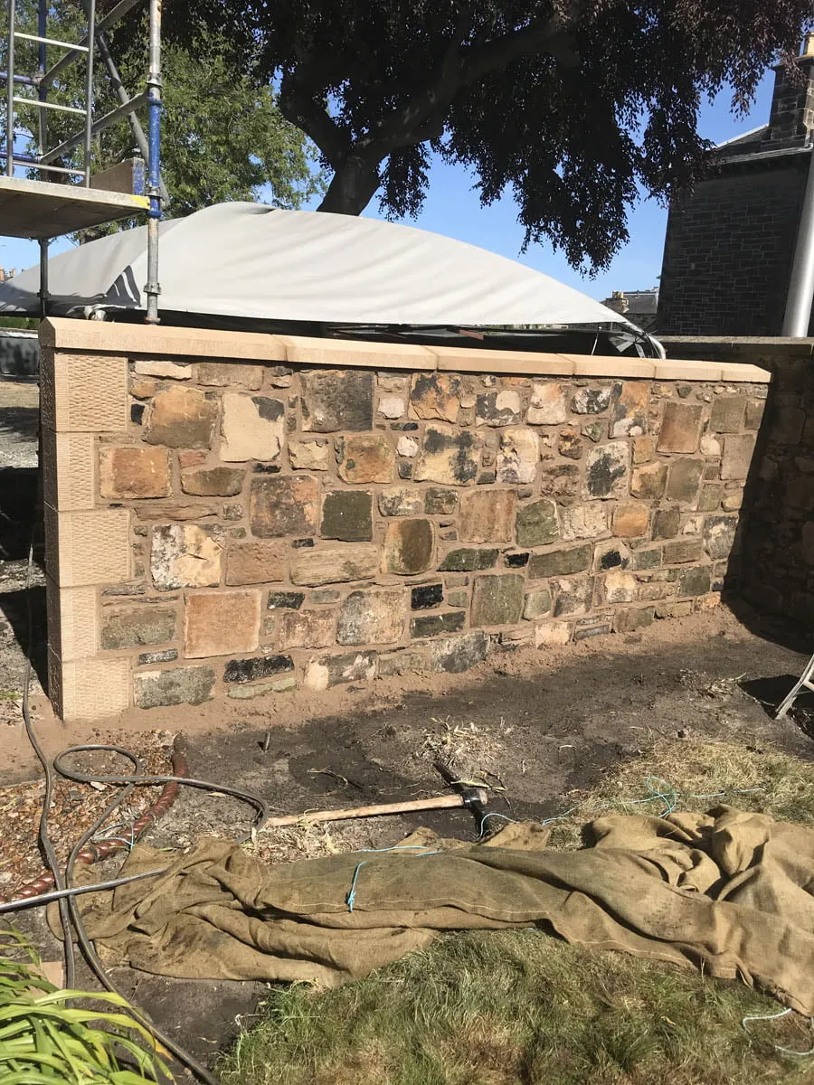 Newly rebuilt stone garden wall with coping stones and scaffolding alongside