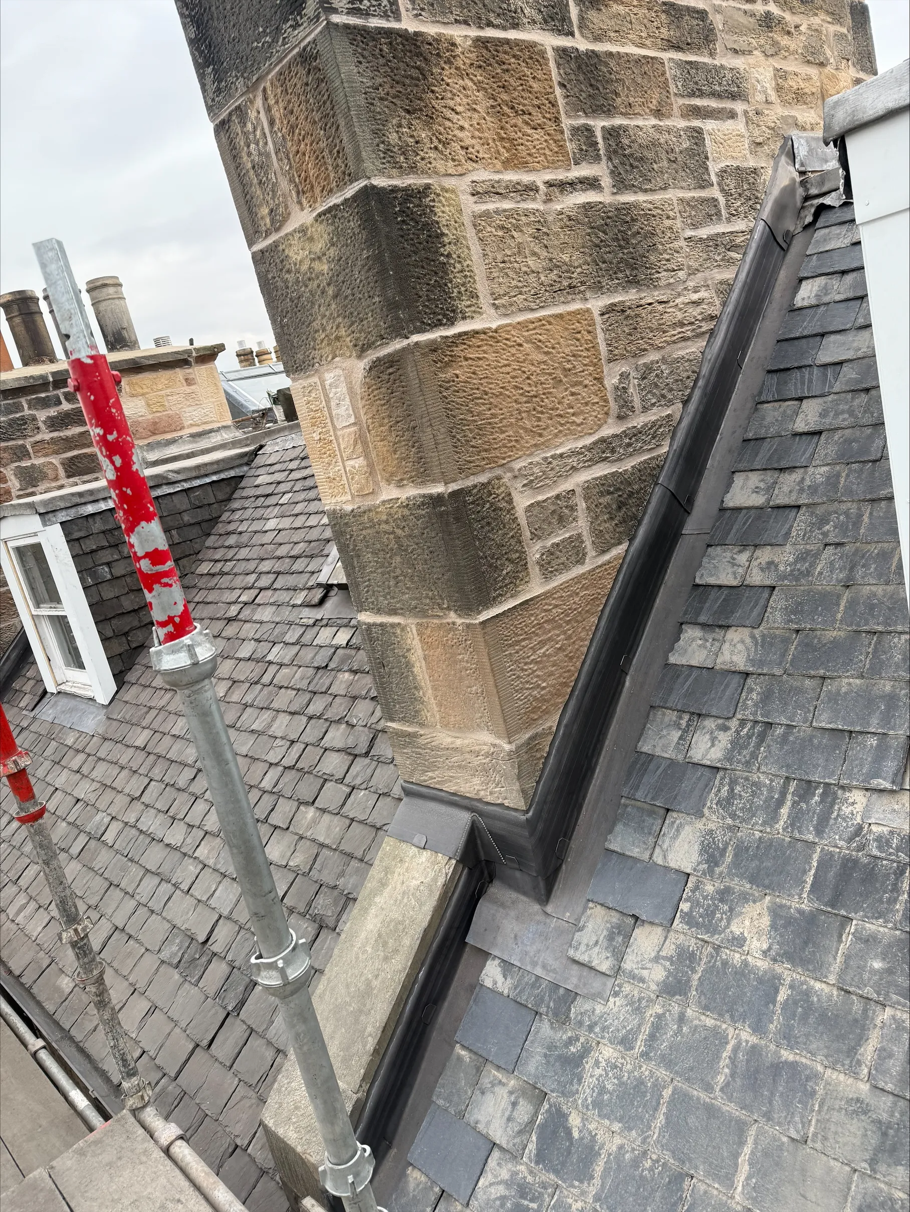 Slate roof meeting a stone wall, with new lead flashing and scaffolding