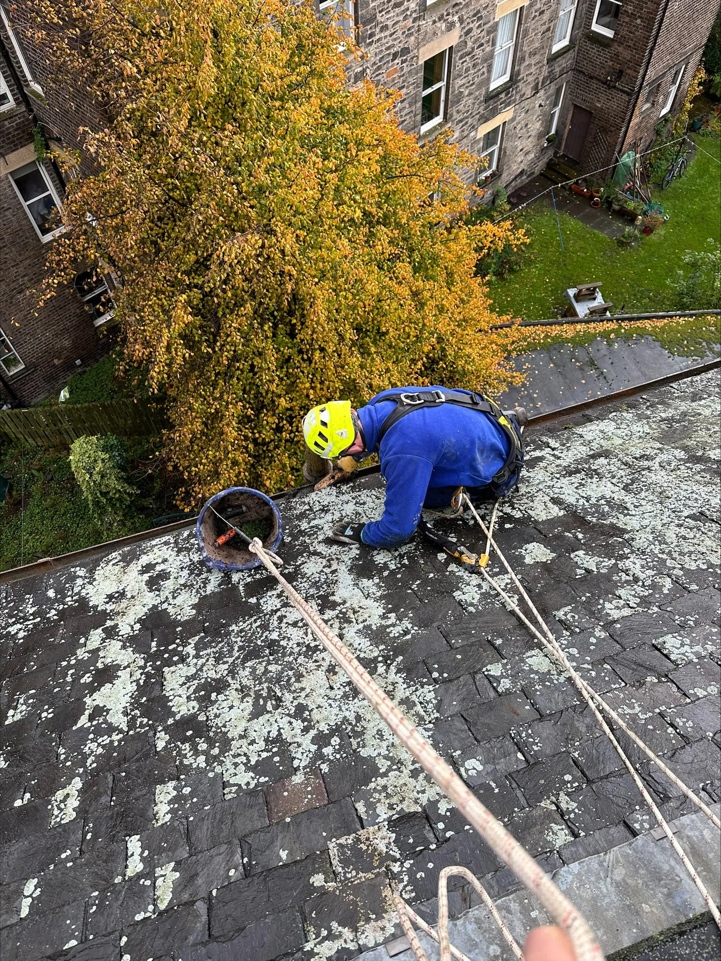 Rope access operative working on a roof above a garden
