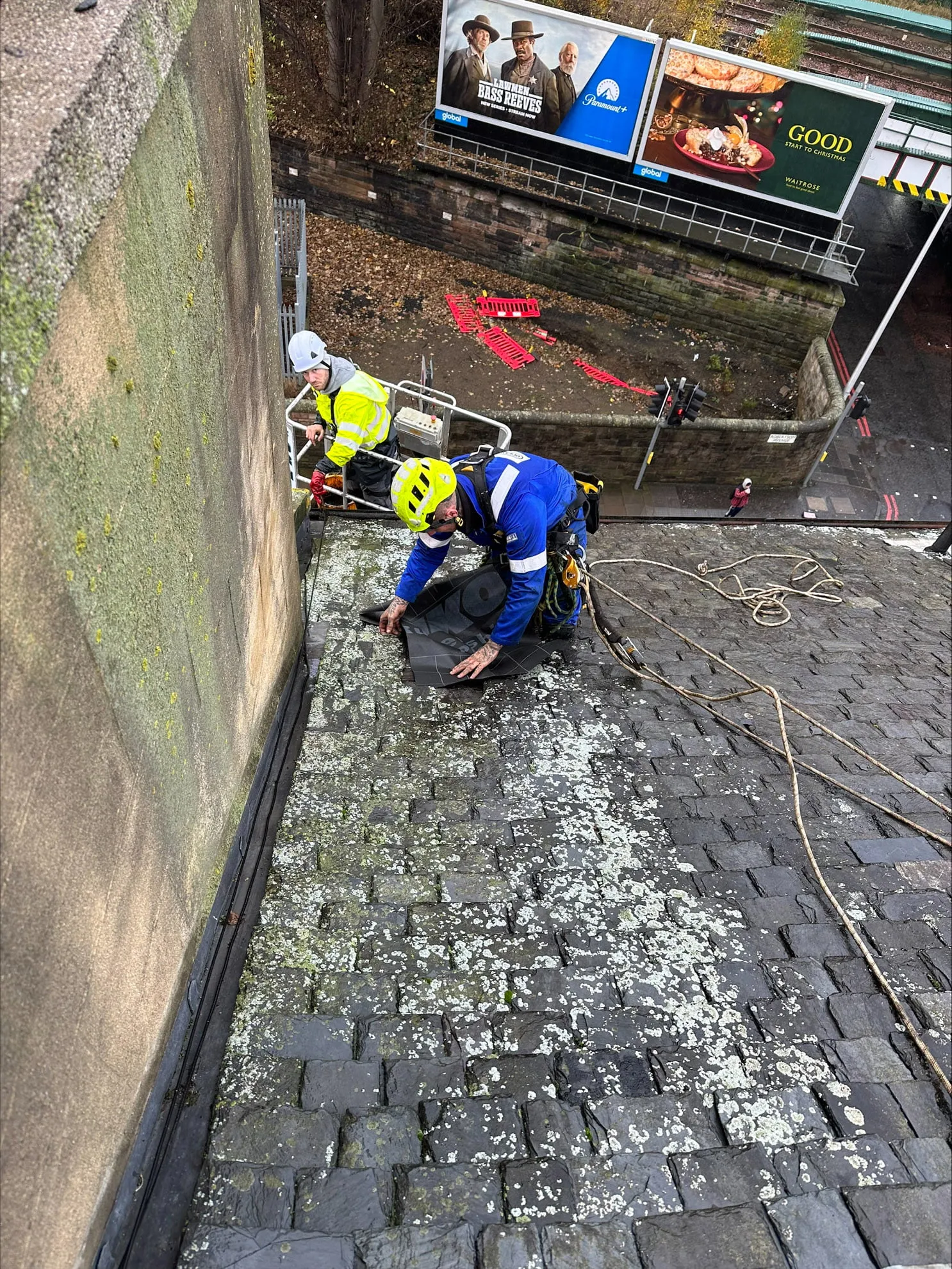 Two operatives working at the base of a stone wall on a cobbled street
