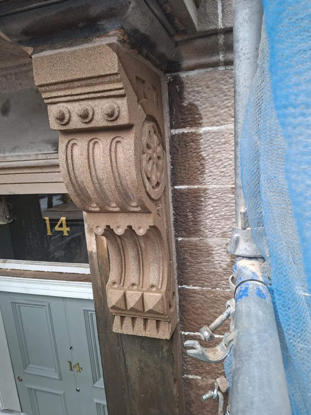 Newly carved sandstone corbel with rosette and fluted scroll detail beside a front door