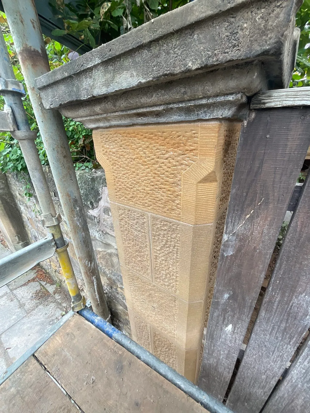 Rebuilt sandstone gate pillar with stugged faces and tooled margins beneath the original cap