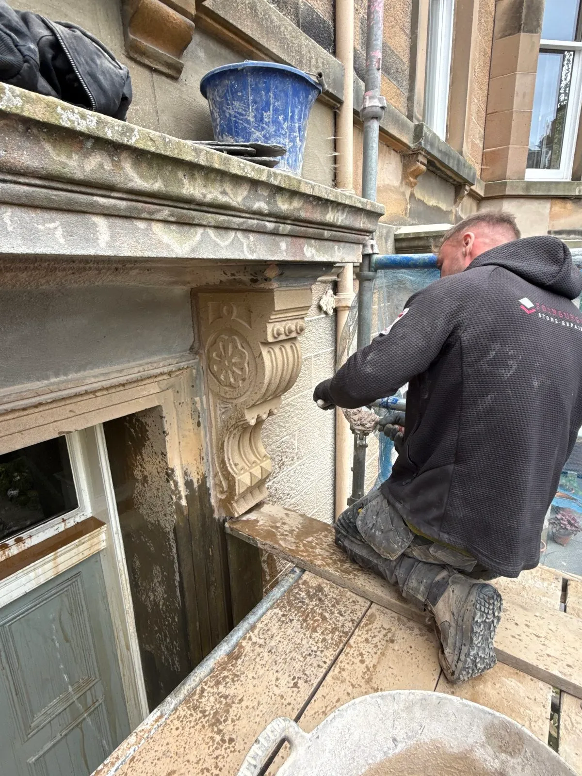 Stonemason fitting a new carved sandstone corbel beside a doorway
