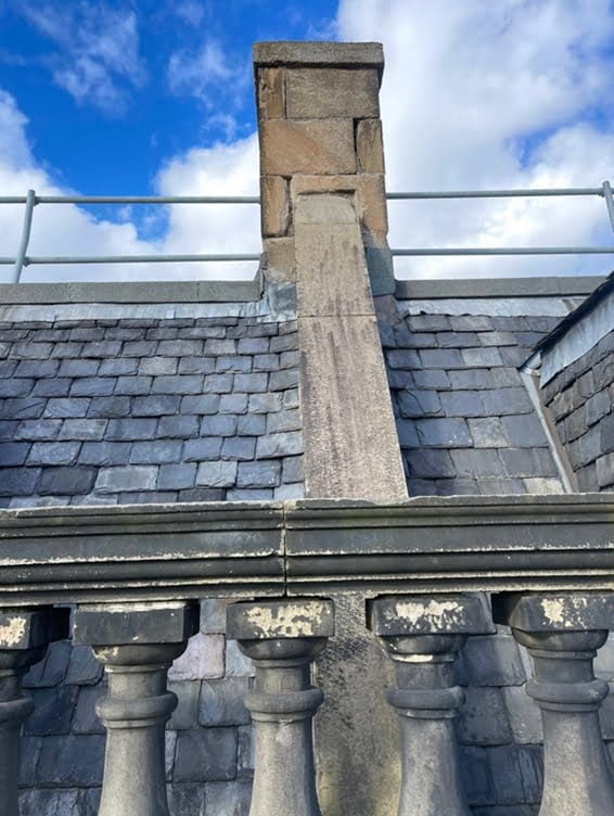 Tall stone chimney stack on a slate roof with scaffolding in place