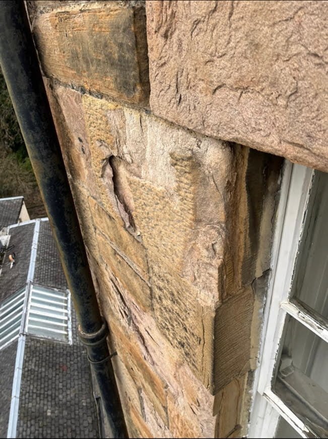 Badly eroded sandstone above a window, with cracked and delaminating blocks